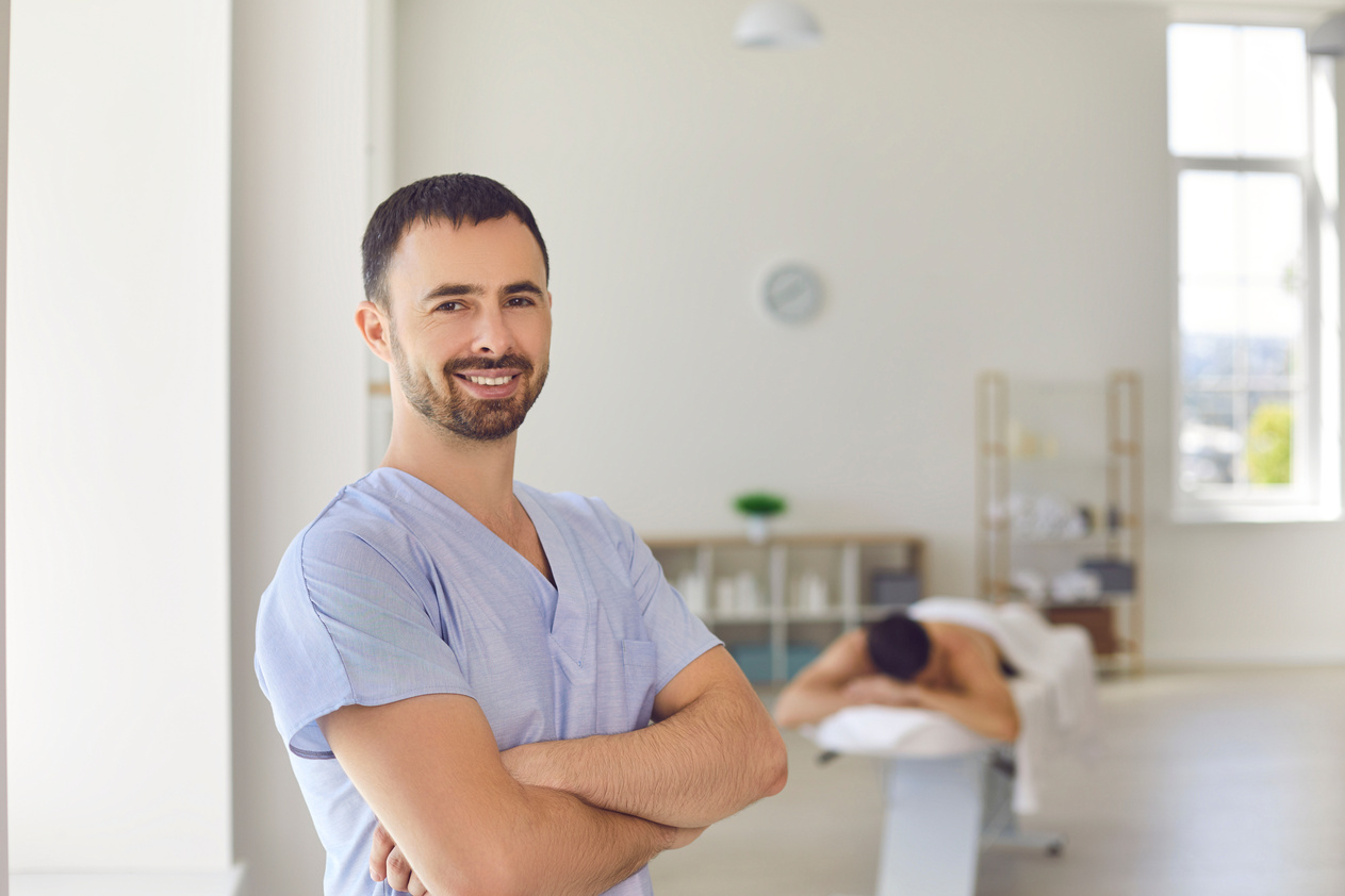 Smiling Masseur or Physiotherapist Standing Arms Folded in Massage Room of Modern Health Center